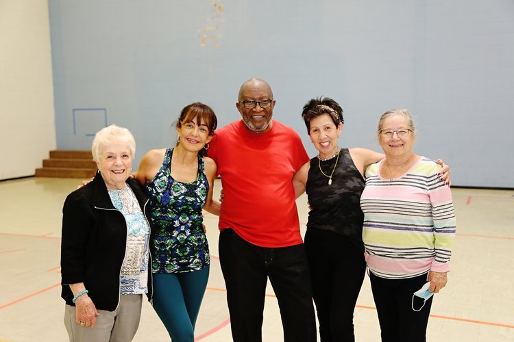 Five adults smiling and posing in a gym setting, wearing casual and workout attire.